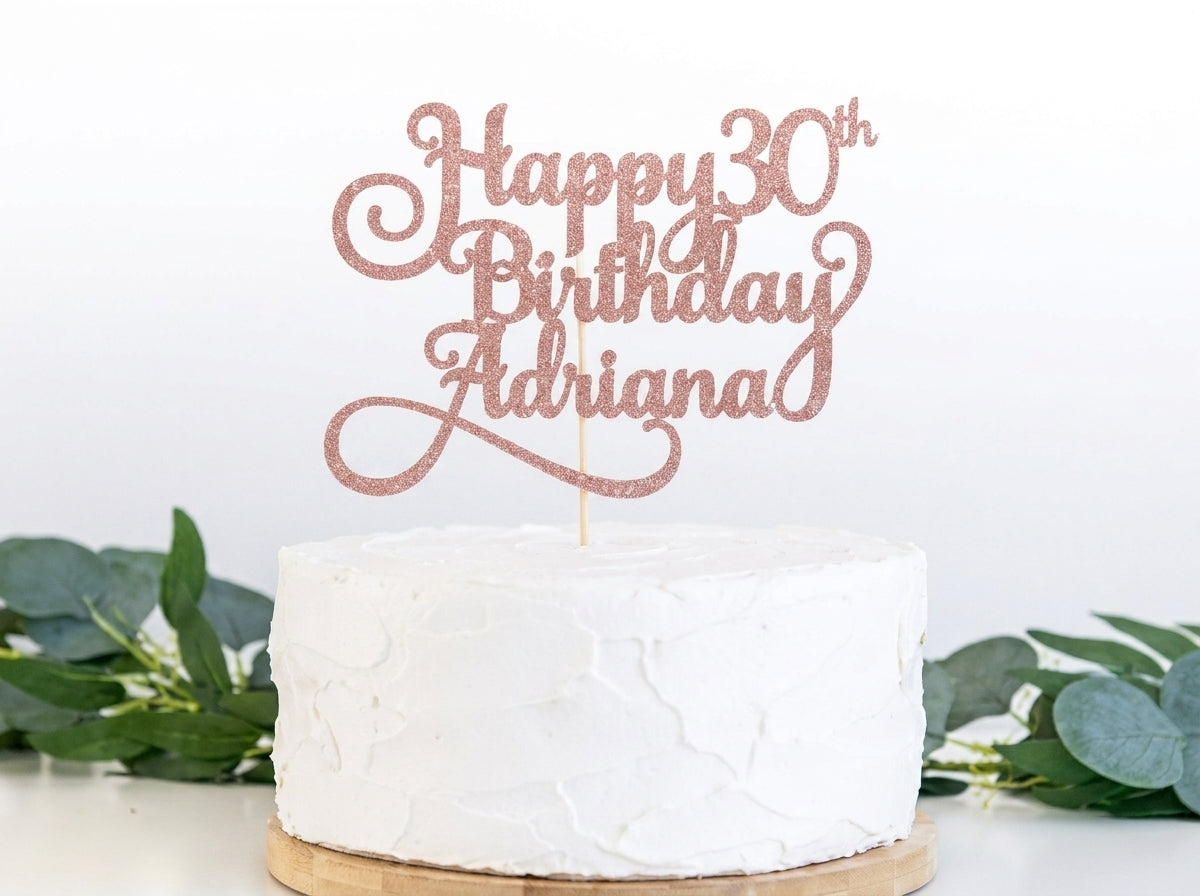Rose gold glitter "Happy 30th Birthday Adriana" cake topper on white frosted cake with green foliage