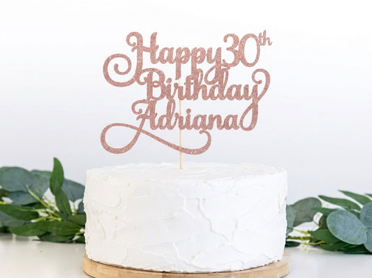 Rose gold glitter "Happy 30th Birthday Adriana" cake topper on white frosted cake with green foliage