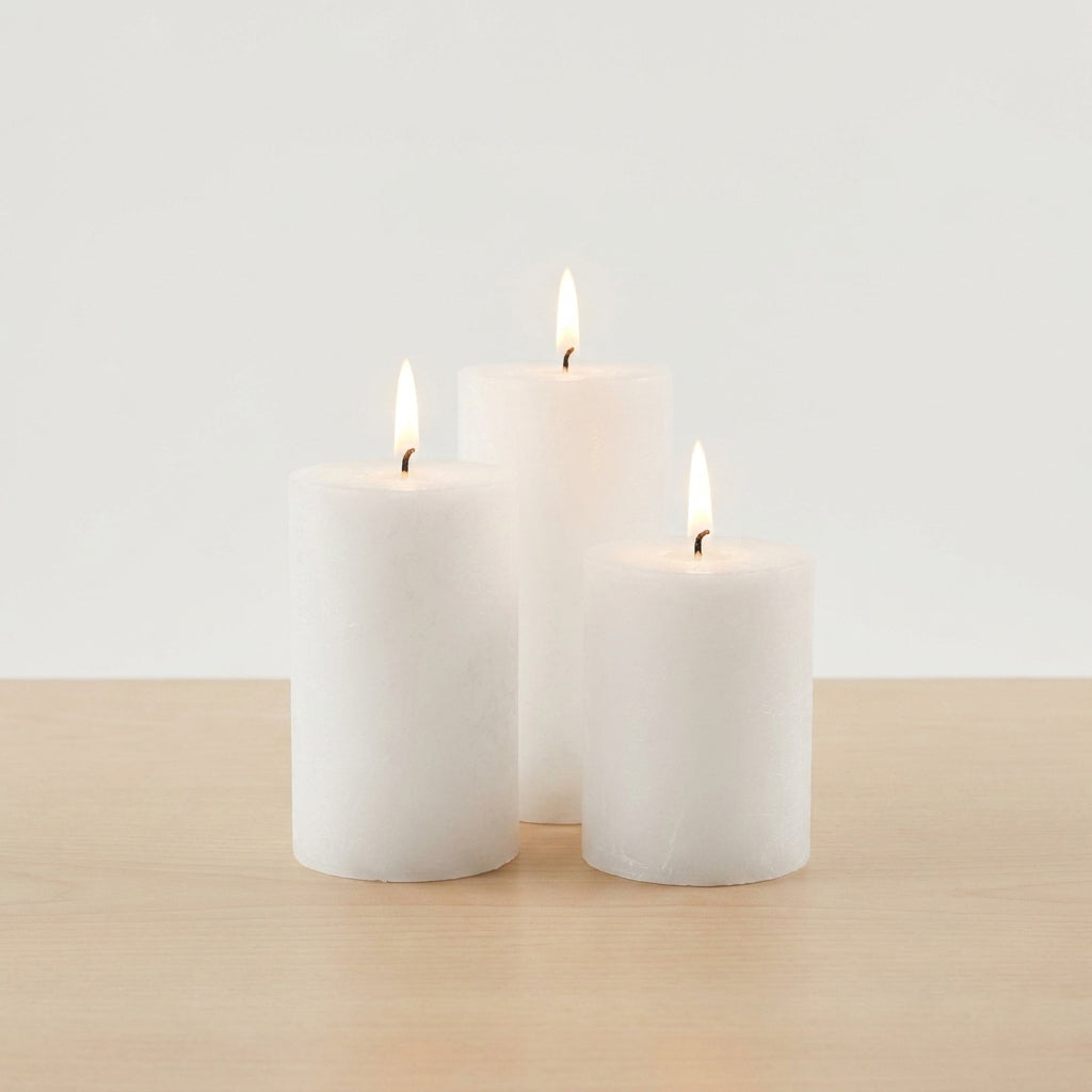 Three white pillar candles of varying heights with lit flames on wooden surface