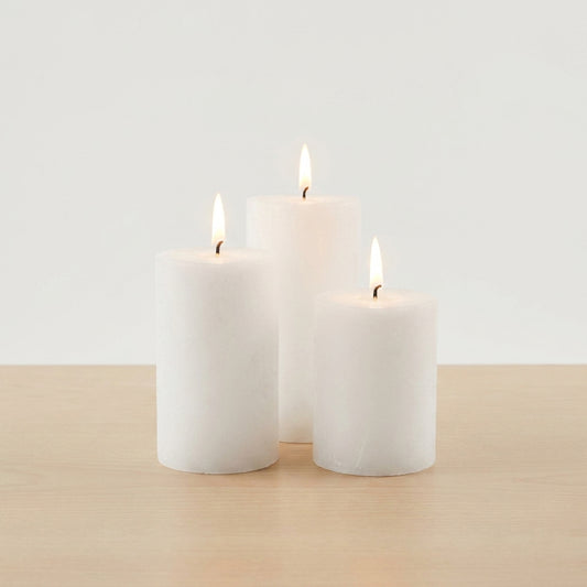 Three white pillar candles of varying heights with lit flames on wooden surface