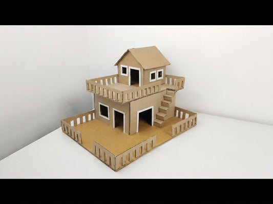 Two-story tan cardboard house model with white window frames, wooden railings, stairs, and rooftop deck
