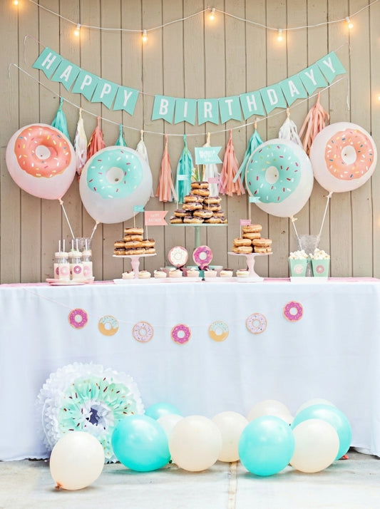 Donut balloon party decoration set with pink, mint green, and cream balloons, banner, tassels, and string lights